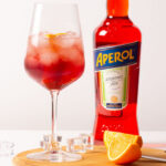 a bottle of aperol with a cocktail and orange slices