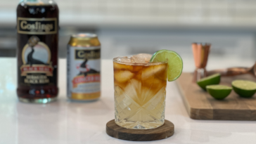 dark n stormy cocktail with goslings rum, ginger beer, and lime in background